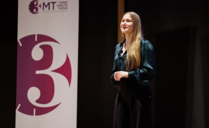 Emily Cooper is the 2023 winner of the UQ 3MT competition. A woman with blonde hair wearing a green blouse and navy pants standing on a stage
